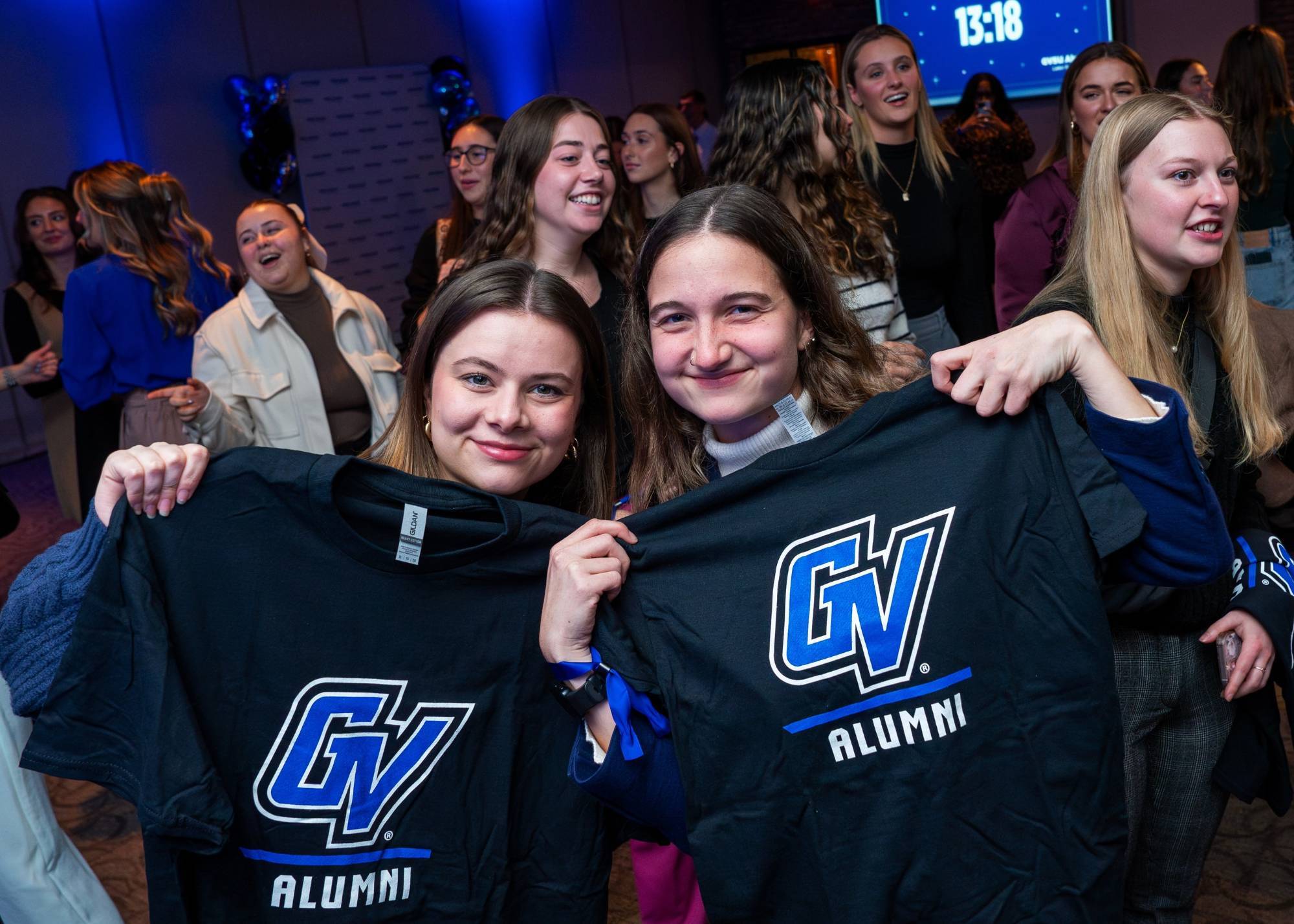 Two grads pose for a photo holding GV Alumni tshirts